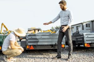 Agronomist with salesman choosing a new farm truck trailer, standing on the open ground of the agricultural shop