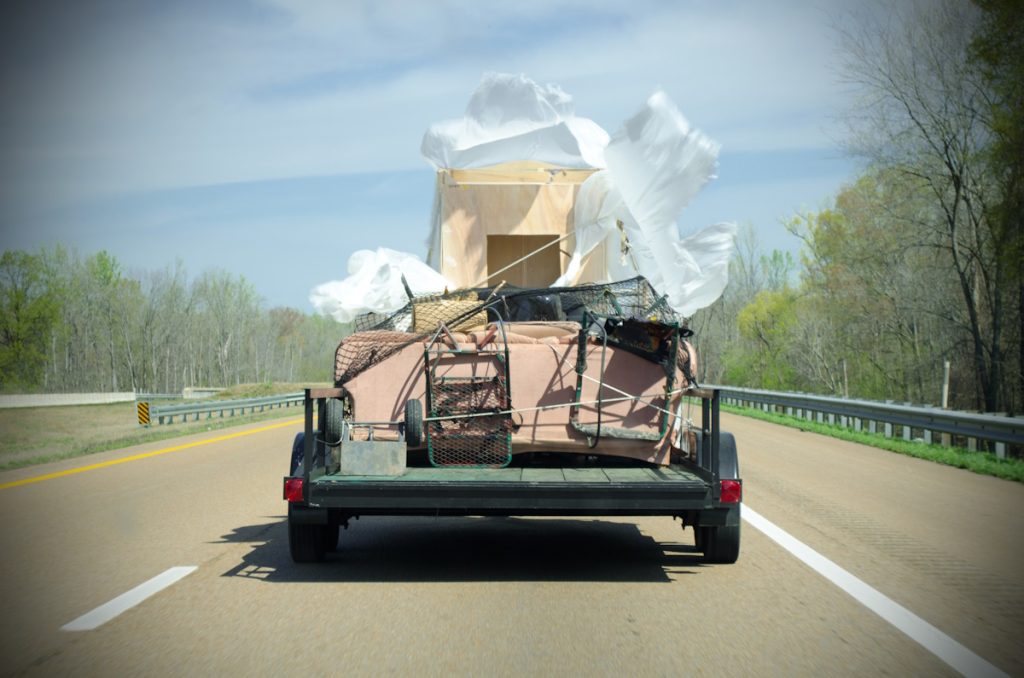 Military green utility trailer hauling loose load of trash and junk.